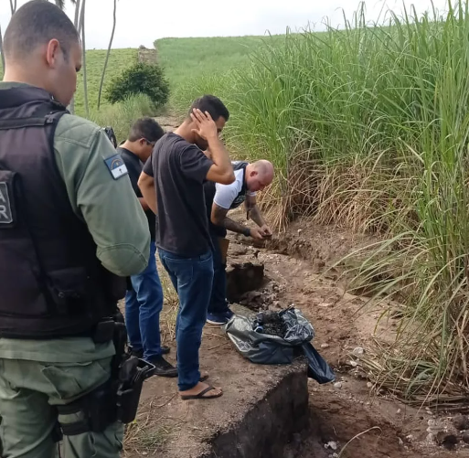 Polícia e, de preto, suspeito de ter mandado assaltarem pais e irmã no local em que corpos das vítimas foram achados, em Nazaré da Mata